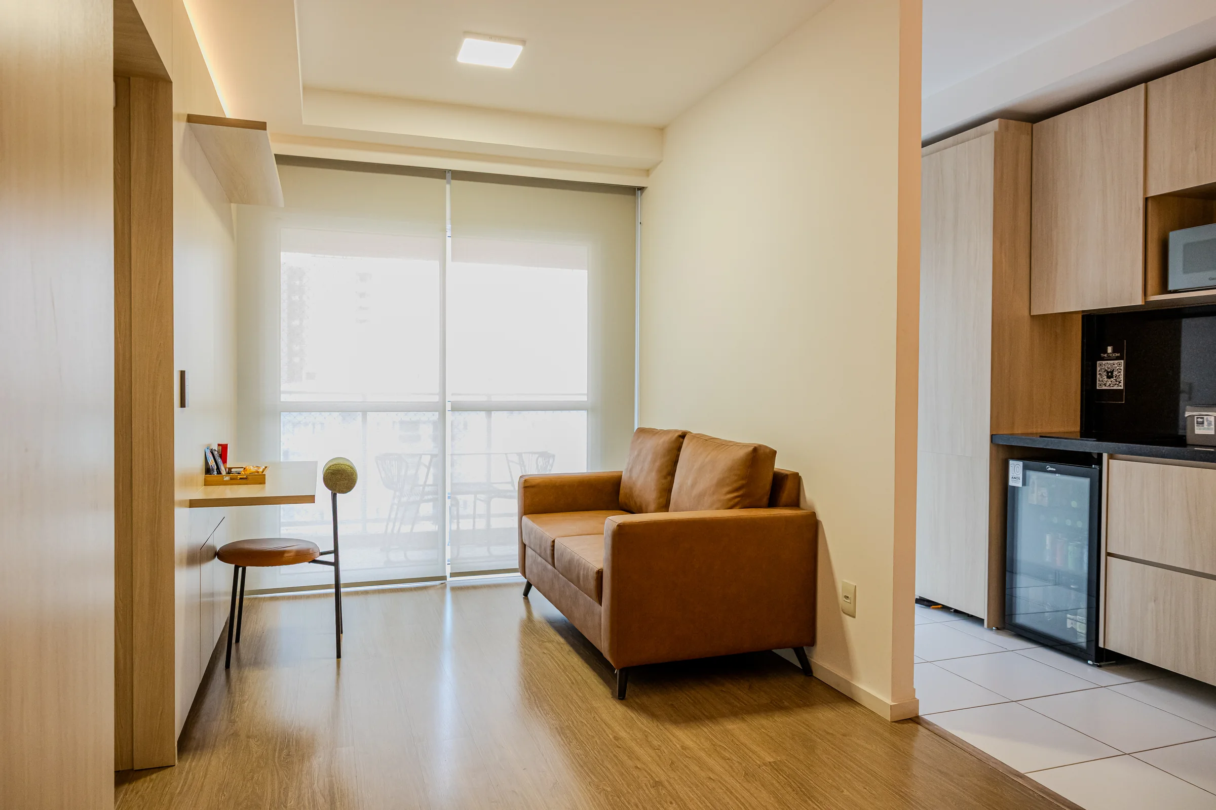 Sala com sofá marrom, bancada de trabalho e janela ampla.