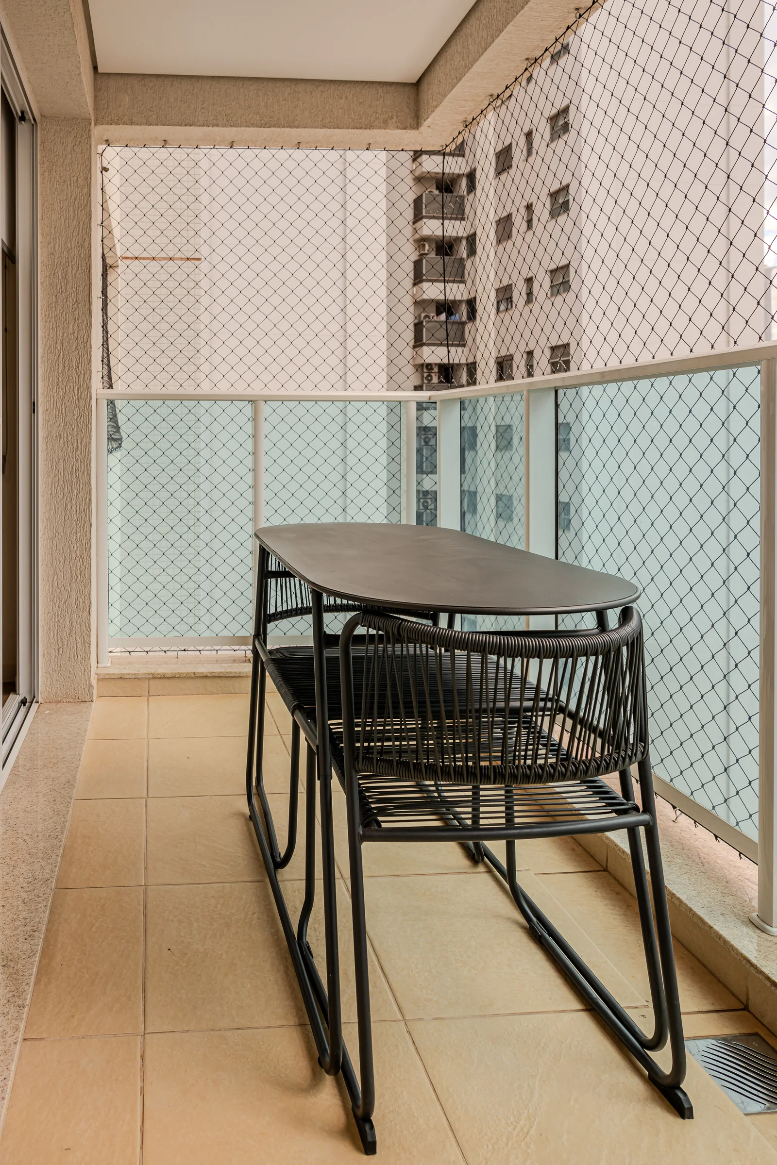 Varanda com mesa, duas cadeiras e tela de proteção.