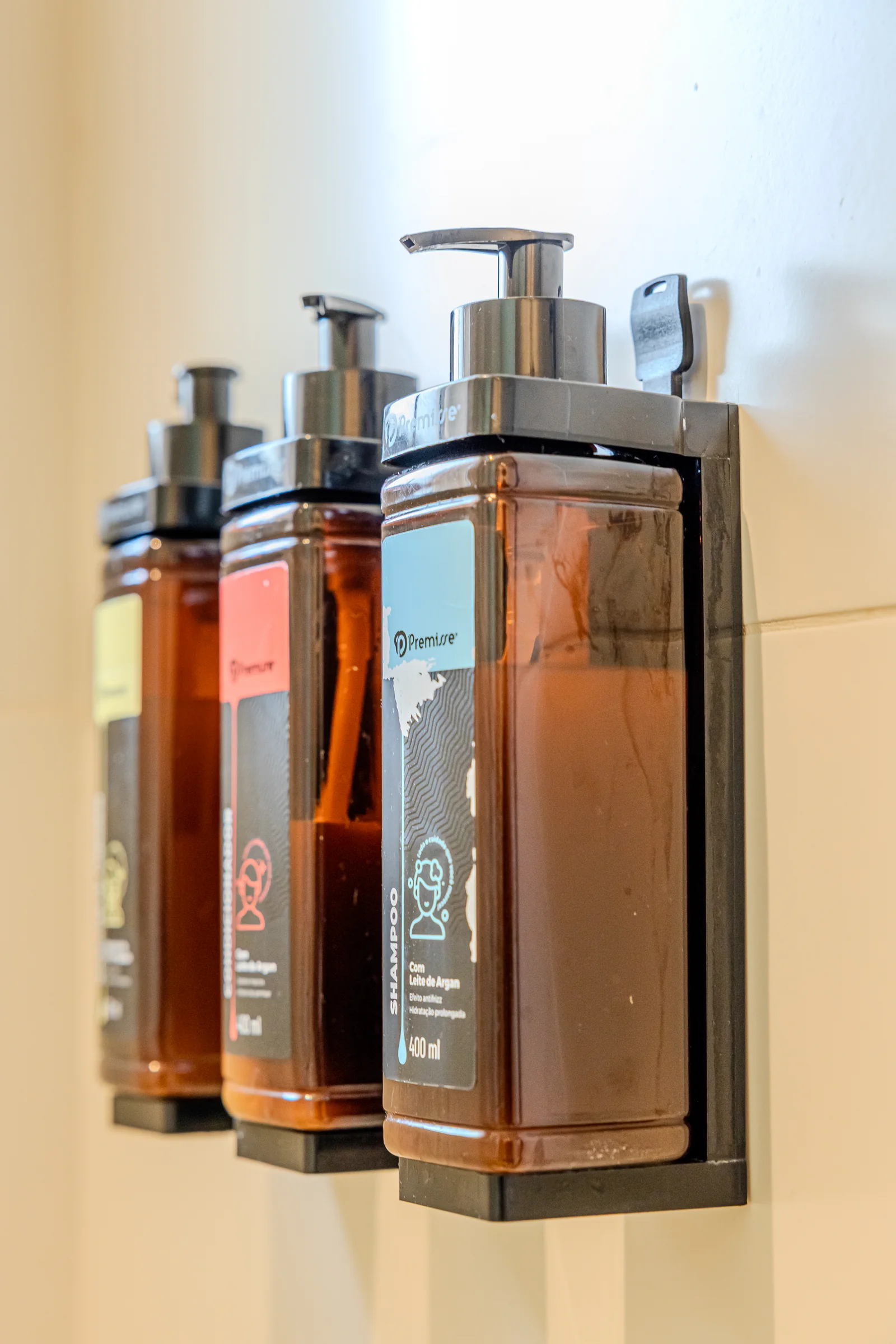 Frascos de shampoo, condicionador e sabonete fixados na parede do box.