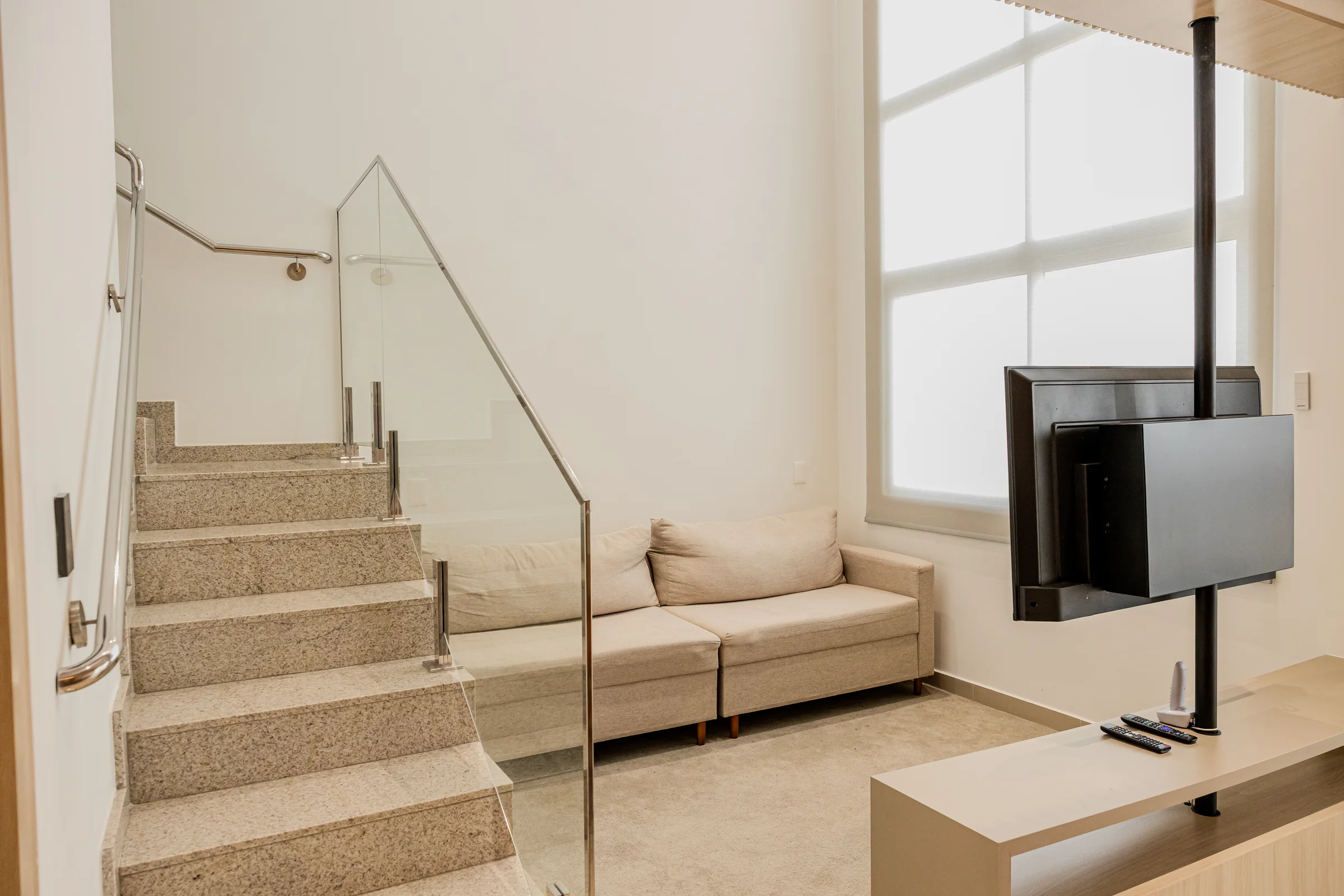 Escada de pedra com guarda-corpo de vidro ao lado da sala.