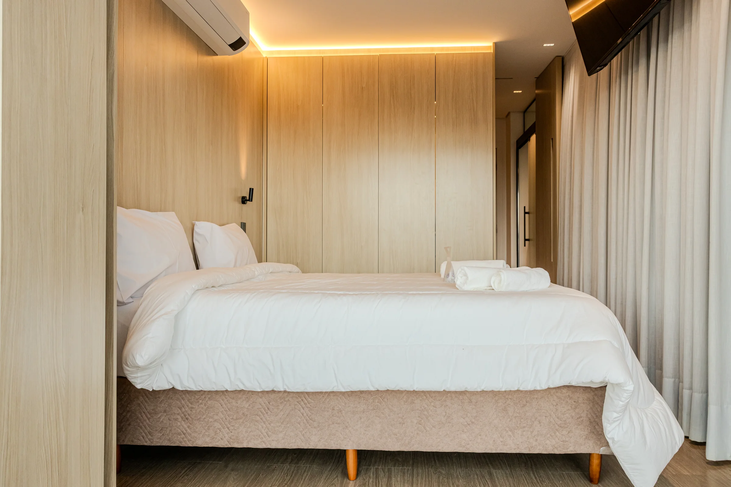 Cama de casal preparada diante de armários de madeira.