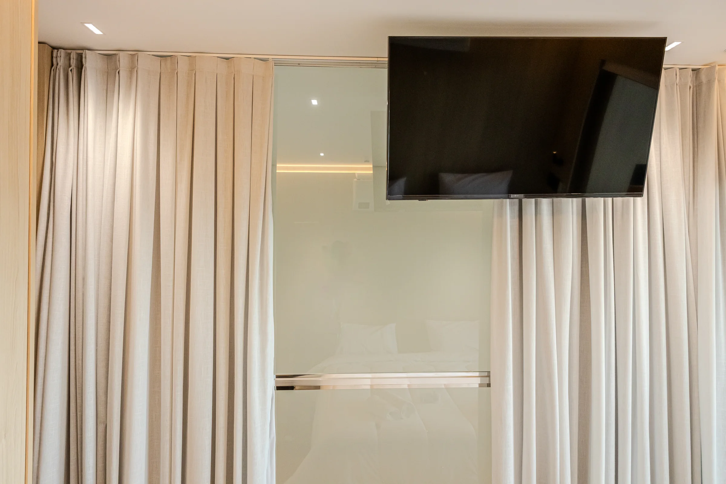Televisão suspensa diante de uma divisória de vidro e cortinas.