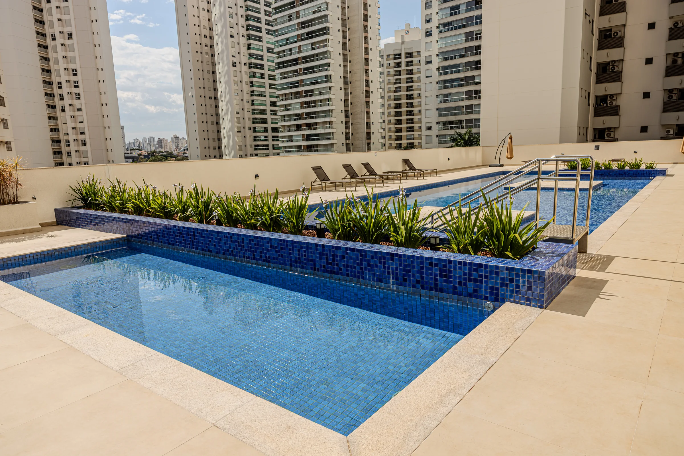 Piscina externa do condomínio com deck e edifícios ao redor.