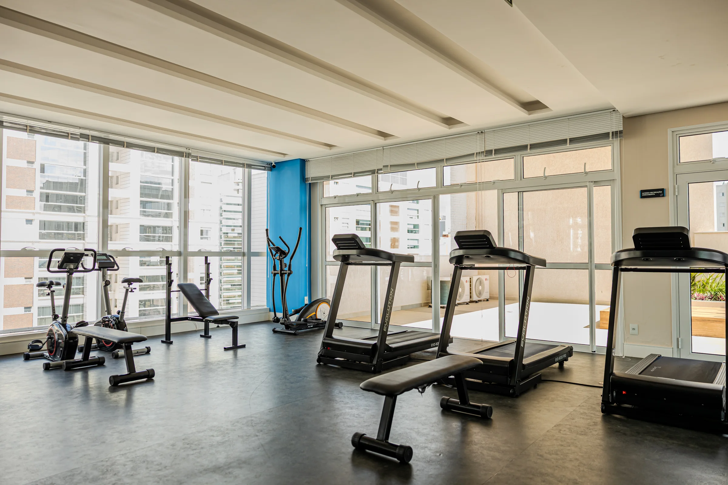 Academia iluminada com esteiras, bicicleta e equipamentos de musculação.